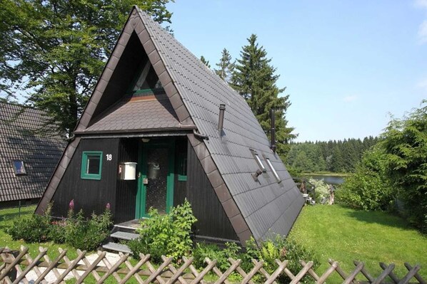 A triangular wooden building with a sloped roof, a green door, and a small porch area.