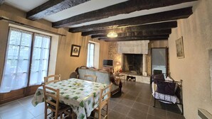 Ein gemütliches Wohnzimmer mit freiliegenden Holzbalken, einem Kamin, einem Esstisch mit Stühlen und einem Fernseher.