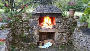 Un horno de piedra al aire libre con fuego encendido, rodeado de follaje y plantas en macetas.