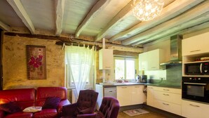 Una sala de estar acogedora con un sofá de cuero rojo y sillones morados, una mesa de centro de madera y una araña. La cocina cuenta con gabinetes blancos, un microondas y una estufa.