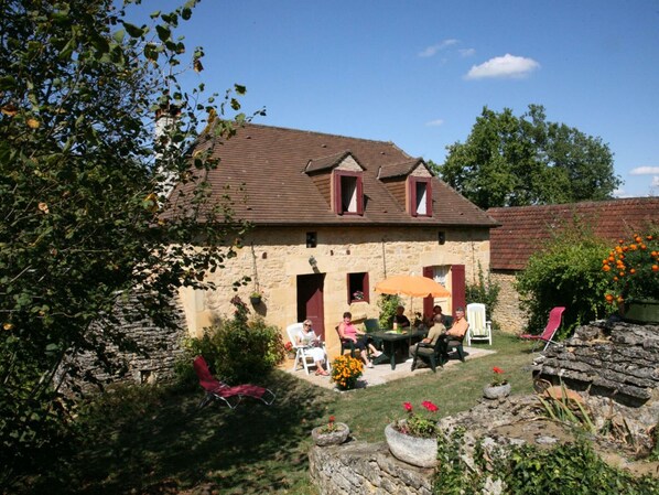 A stone house with a tiled roof, a patio with outdoor seating, and a garden with potted plants and flowers. - Charming house in Dordogne with garden and fireplace (Sainte-Mondane)