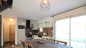 A modern kitchen with a wooden dining table and chairs, a built-in oven, and a large window.