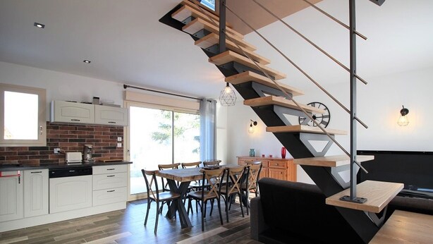 A modern kitchen with white cabinets, a brick backsplash, and a dining area with a wooden table and chairs.