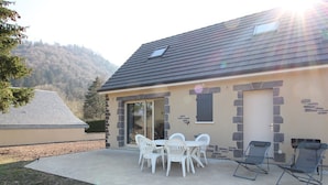 A house with a patio, stone walls, and a view of a forested hill.