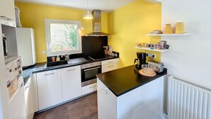 A compact kitchen with white cabinets, a black countertop, a window with a view of greenery, and a white radiator. - Modern downtown apartment, 600m from beach, secure residence, parking (Granville)