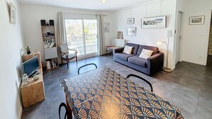 A living room with a sofa, a dining table, and a chair. There is a bookshelf and a lamp. - Modern downtown apartment, 600m from beach, secure residence, parking (Granville)