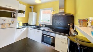A compact kitchen with white cabinets, a black countertop, a stainless steel range hood, and a window with a view of the outside. - Modern downtown apartment, 600m from beach, secure residence, parking (Granville)