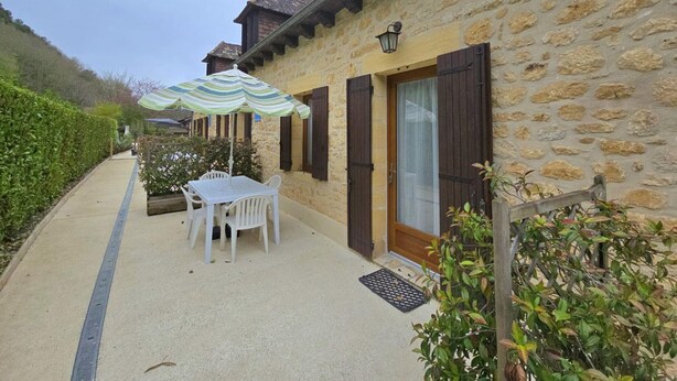 A stone building with a covered patio, a table with chairs, and a door with shutters. - Charming house in Domme with WiFi near the Dordogne (Domme)