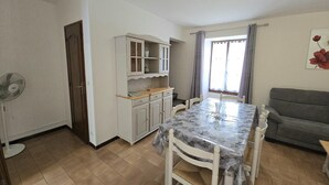 A compact living space with a dining table and chairs, a kitchenette with cabinets, a sofa, and a window with curtains. - Charming house in Domme with WiFi near the Dordogne (Domme)