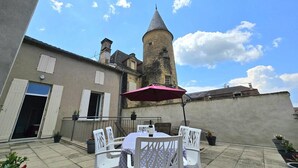 An outdoor patio with a table and chairs, a pink umbrella, and a view of a historic tower. - House with rooftop terrace in the heart of Périgord (Villefranche-du-Périgord)