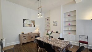 A dining area with a wooden table, chairs, a hanging light fixture, and a white wall with shelves. - House with rooftop terrace in the heart of Périgord (Villefranche-du-Périgord)