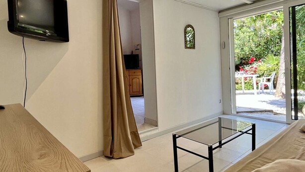 A modern living room with a flat-screen TV, a glass coffee table, and a sliding glass door leading to a garden.
