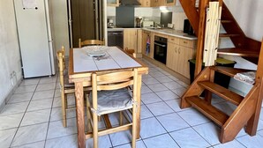 A compact kitchen with wooden cabinets, a dining table, and a staircase.