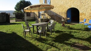 A stone building with a staircase leading to an entrance, a covered outdoor seating area with chairs and a table, and a grassy yard. - Charming Countryside Retreat with Fireplace, Garden, and Family Amenities in Tourtoirac, France (Tourtoirac)
