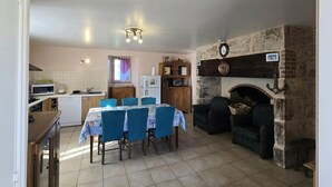 A compact kitchen with a dining area, a stone fireplace, and a small seating area. - Charming Countryside Retreat with Fireplace, Garden, and Family Amenities in Tourtoirac, France (Tourtoirac)