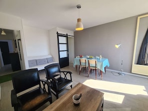 A room with a dining area, a sofa, and a table with a remote control.