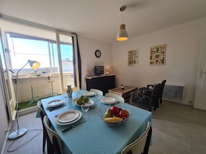 A dining area with a table set for four, a TV on a cabinet, and artwork on the wall.