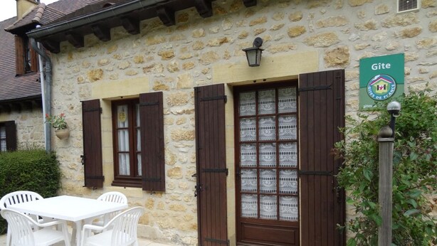 A stone building with a wooden door and shutters, a sign indicating 'Gîte', and a table with chairs outside. - Charming house near Domme with Wifi, 2 bedrooms (Domme)