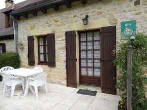 A stone building with a wooden door and shutters, a sign indicating 'Gîte', and a table with chairs outside. - Charming house near Domme with Wifi, 2 bedrooms (Domme)