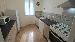 A compact kitchen with a microwave, sink, stove, and a window with curtains. - Charming house near Domme with Wifi, 2 bedrooms (Domme)