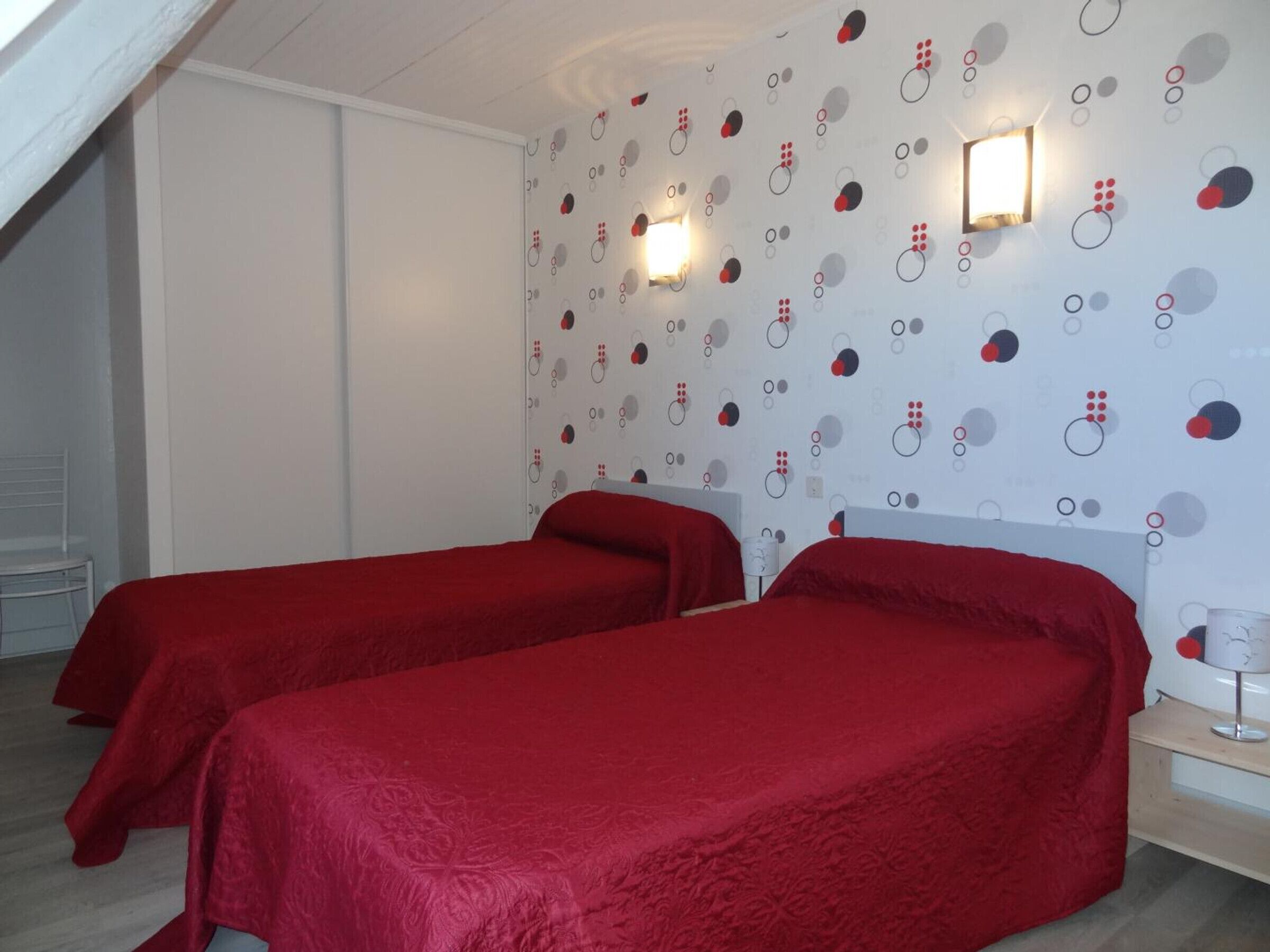 Une chambre avec deux lits recouverts de draps rouges, un mur à motifs et deux lampes fixées au mur.