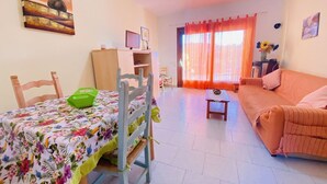 Un saló amb un sofà, taula de dinar amb caires, taula petita amb un vas i finestra amb cortines.