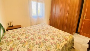 Une chambre à coucher avec une couvre-lit à motifs floraux, une armoire en bois et une table de chevet avec une lampe.
