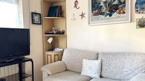 A living room with a flat-screen TV, a beige sofa, a wooden bookshelf, and a framed painting. - M282 - Marcelli, three-room apartment with garden 100m from the sea (Marcelli)