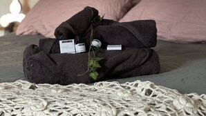 Ein ordentlich bezogenes Bett mit einer Spitzendecke, dunklen Handtüchern und einer kleinen Pflanze.