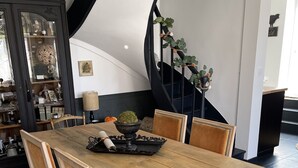 Ein Essbereich mit Holztisch, gepolsterten Stühlen, einer schwarzen Metalltreppe und einem dekorativen Schrank.