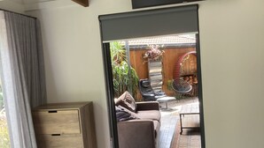 A modern room with a large bed, a wooden dresser, a TV mounted on the wall, and a view of an outdoor patio area. - thespaceperth- the funkiest bali style villa in Perth (Maida Vale)