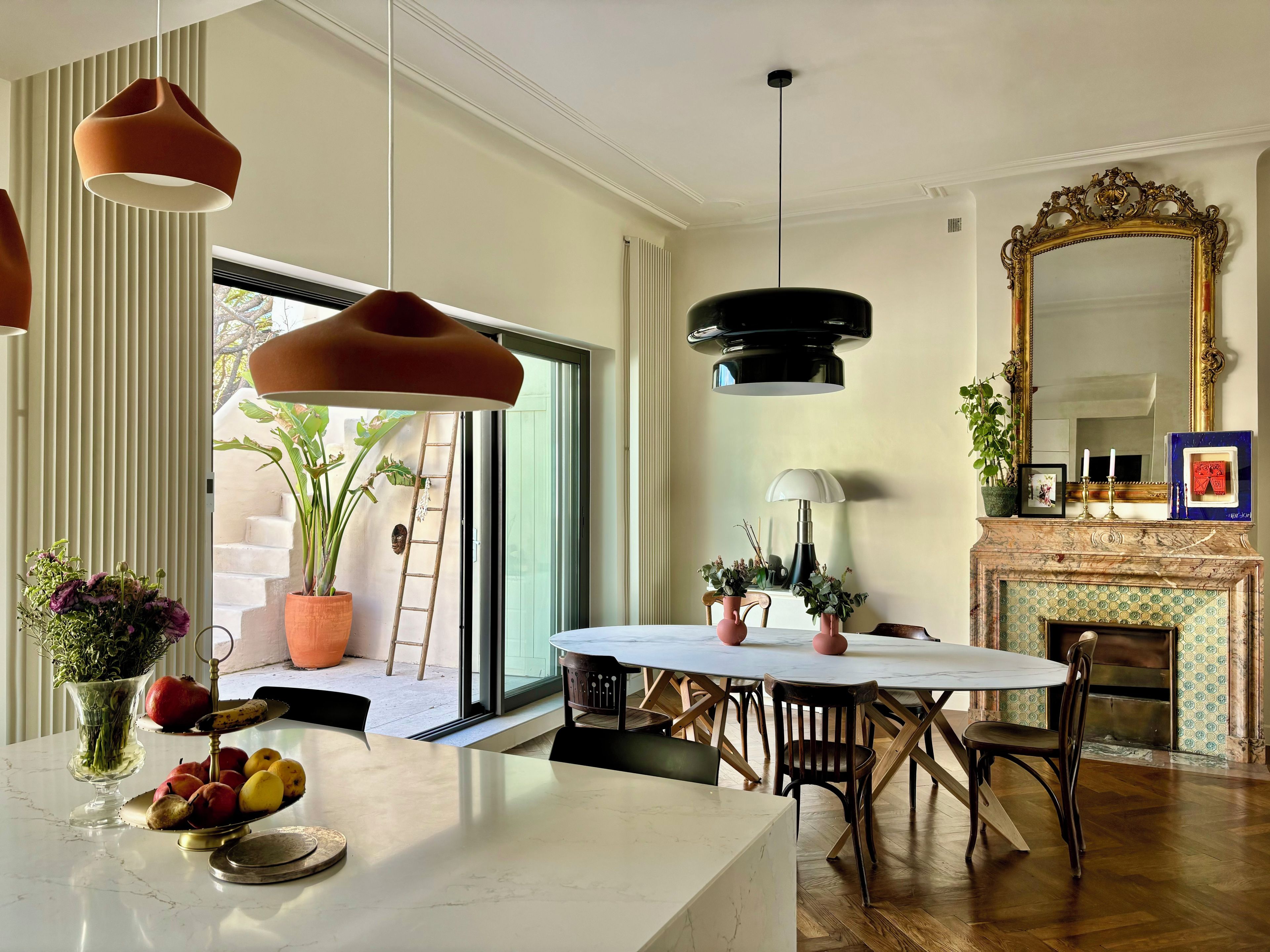 A dining area with a marble table, wooden chairs, pendant lighting, a fireplace, and a large mirror.