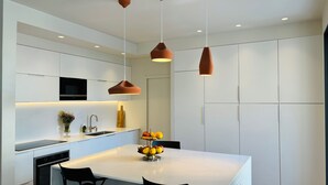 A modern kitchen with white cabinets, a central island with chairs, pendant lighting, and a fruit bowl. - House facing the sea, bright, air-conditioned, terrace, family, calanques (Marseille)
