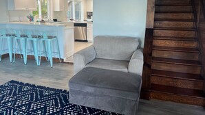 A modern kitchen with white cabinets, a grey sofa, and a patterned rug.