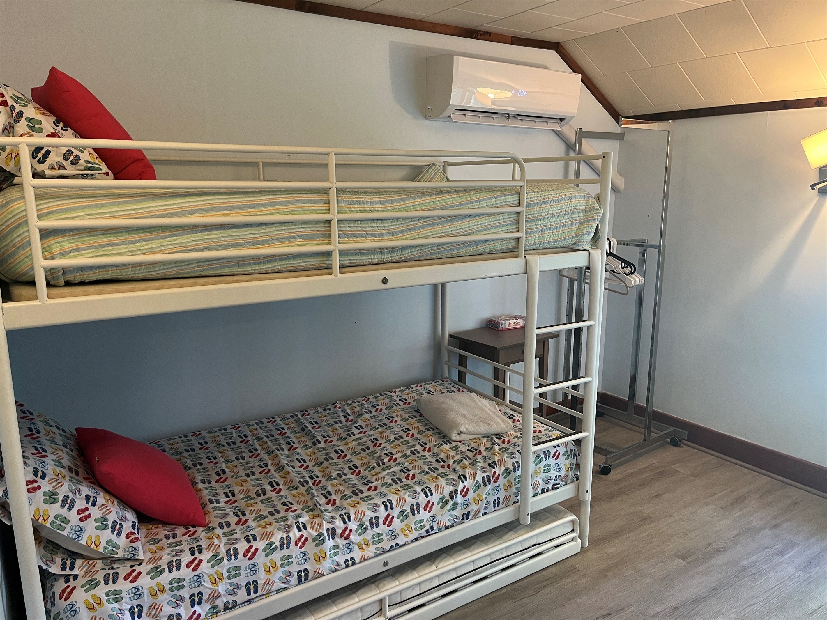 A bunk bed room with a white metal frame, a patterned mattress, and a red pillow.