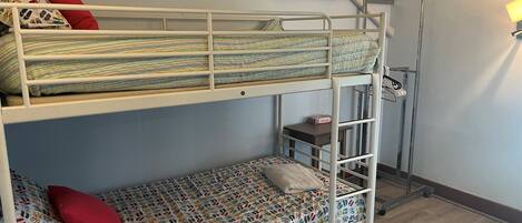 A bunk bed room with a white metal frame, a patterned mattress, and a red pillow.