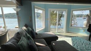 A living room with a large window overlooking a lake, a sofa with cushions, and a patterned rug.