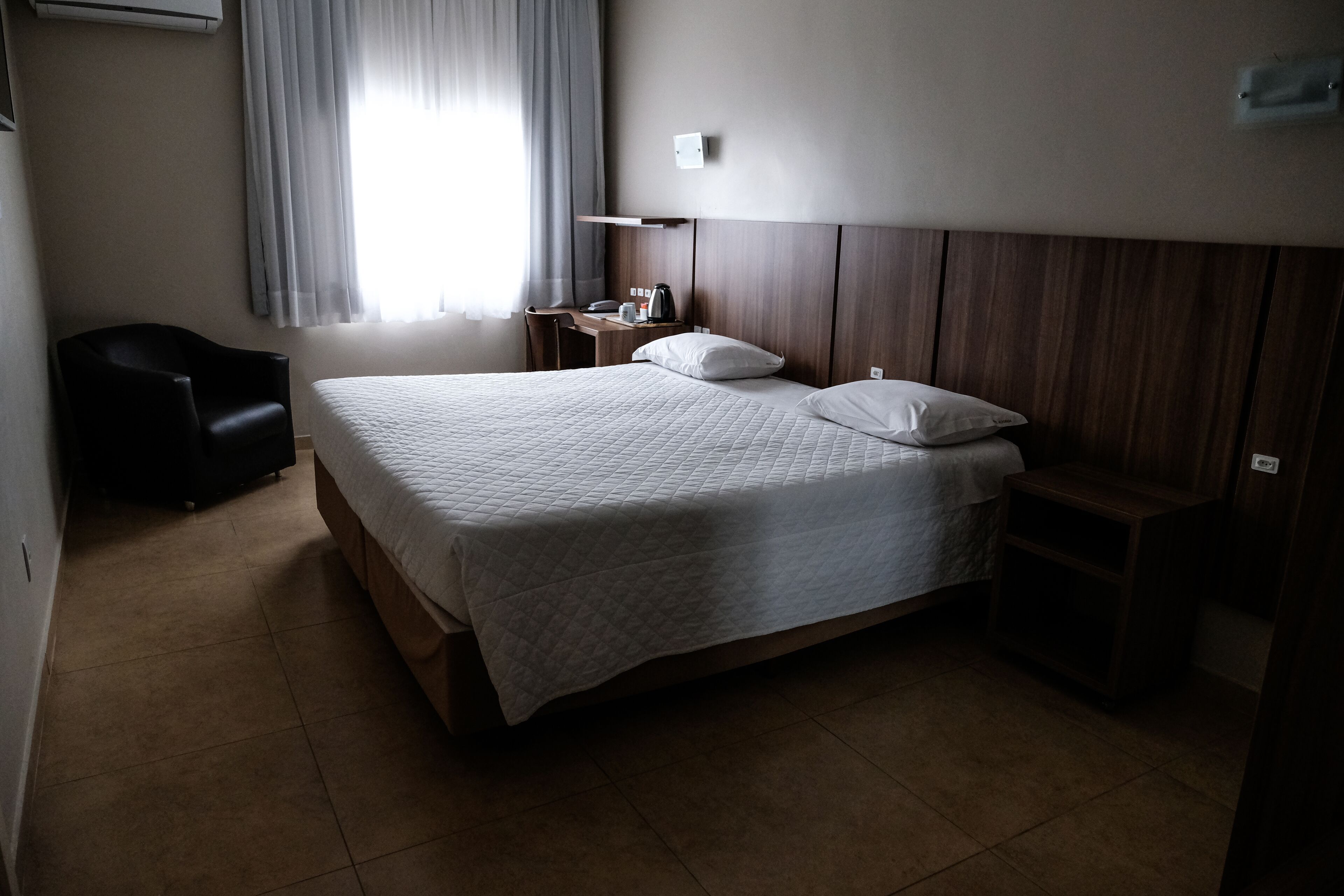 Habitación de hotel con una cama grande, un escritorio, una silla, una mesita de noche y una ventana con cortinas.