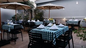 An outdoor dining area with checkered tablecloths, black chairs, and large umbrellas. Tables are set with white napkins and glassware. - Hotel Alvorada (Concordia)