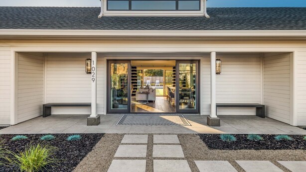 A modern building with a large glass entrance, a covered patio area, and a well-maintained outdoor space with stepping stones and plants.