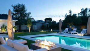 A modern outdoor pool area with a fire feature, lounge chairs, and a well-maintained lawn.