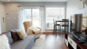 Una sala de estar con un sofá, una silla, un televisor y una mesa de comedor.