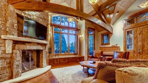 Un salon chaleureux avec une cheminée en pierre, des poutres en bois et de grandes fenêtres donnant sur la forêt.