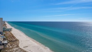 En strand med en klarblå himmel, en sandstrand och en brygga som sträcker sig ut i havet.