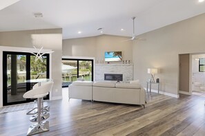 A spacious living area with a large sofa, a bar stool, and a fireplace. - Stunning Home | Pool, Dock & Direct Gulf Access (Marco Island)