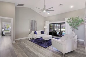 A modern living room with a white sofa, a coffee table, and a large window overlooking a pool. - Stunning Home | Pool, Dock & Direct Gulf Access (Marco Island)