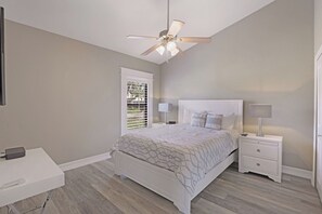 A bedroom with a bed, nightstands, a desk, a ceiling fan, and a window with blinds. - Stunning Home | Pool, Dock & Direct Gulf Access (Marco Island)