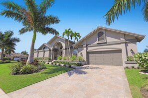 A modern two-story house with a stone driveway, palm trees, and a well-maintained lawn. - Stunning Home | Pool, Dock & Direct Gulf Access (Marco Island)