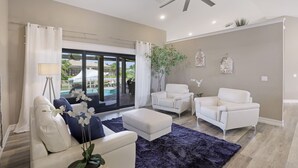 A spacious living room with a ceiling fan, a large window with a view of a pool, and two white sofas with a dark rug. - Stunning Home | Pool, Dock & Direct Gulf Access (Marco Island)