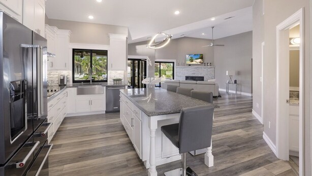 A modern kitchen with white cabinetry, a central island, and a dining area. - Stunning Home | Pool, Dock & Direct Gulf Access (Marco Island)